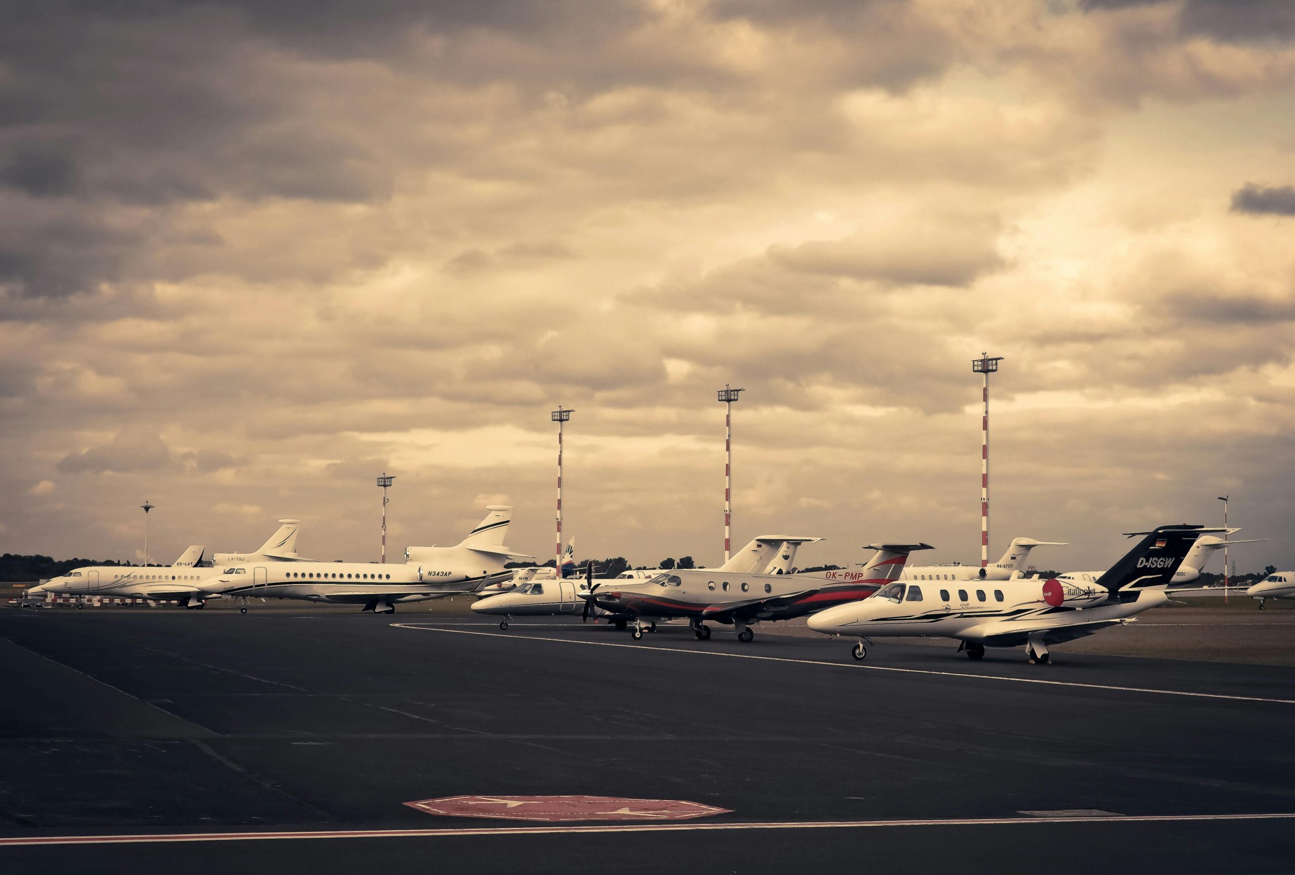 Line of private jets parked on the tarmac under a dramatic cloudy sky, showcasing aviation and travel.