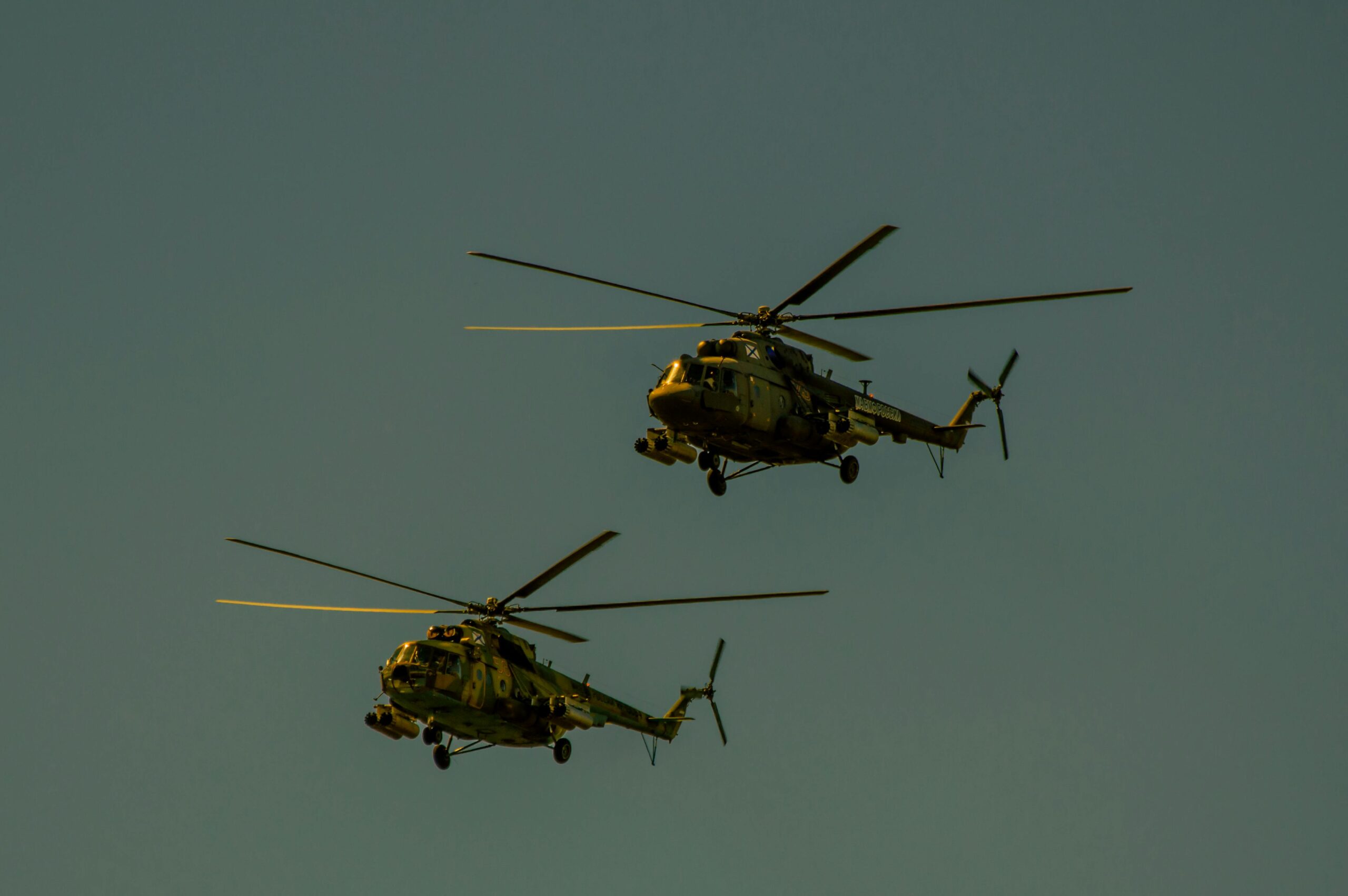 A pair of camouflage military helicopters flying against a clear blue sky.