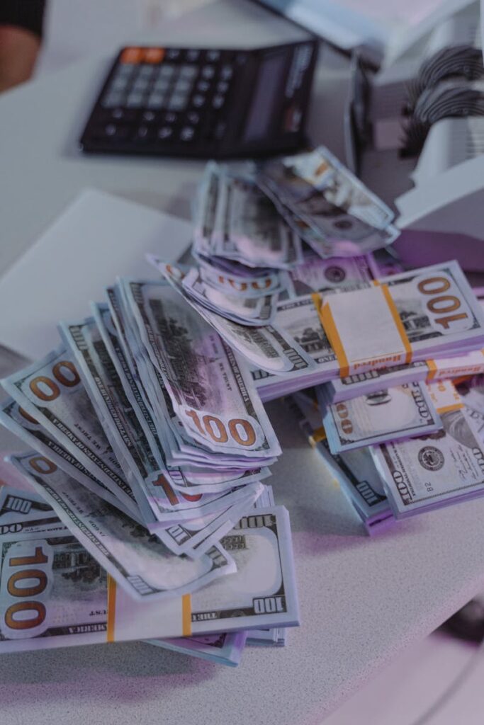 A close-up view of stacked US dollar bills next to a calculator and money counter.