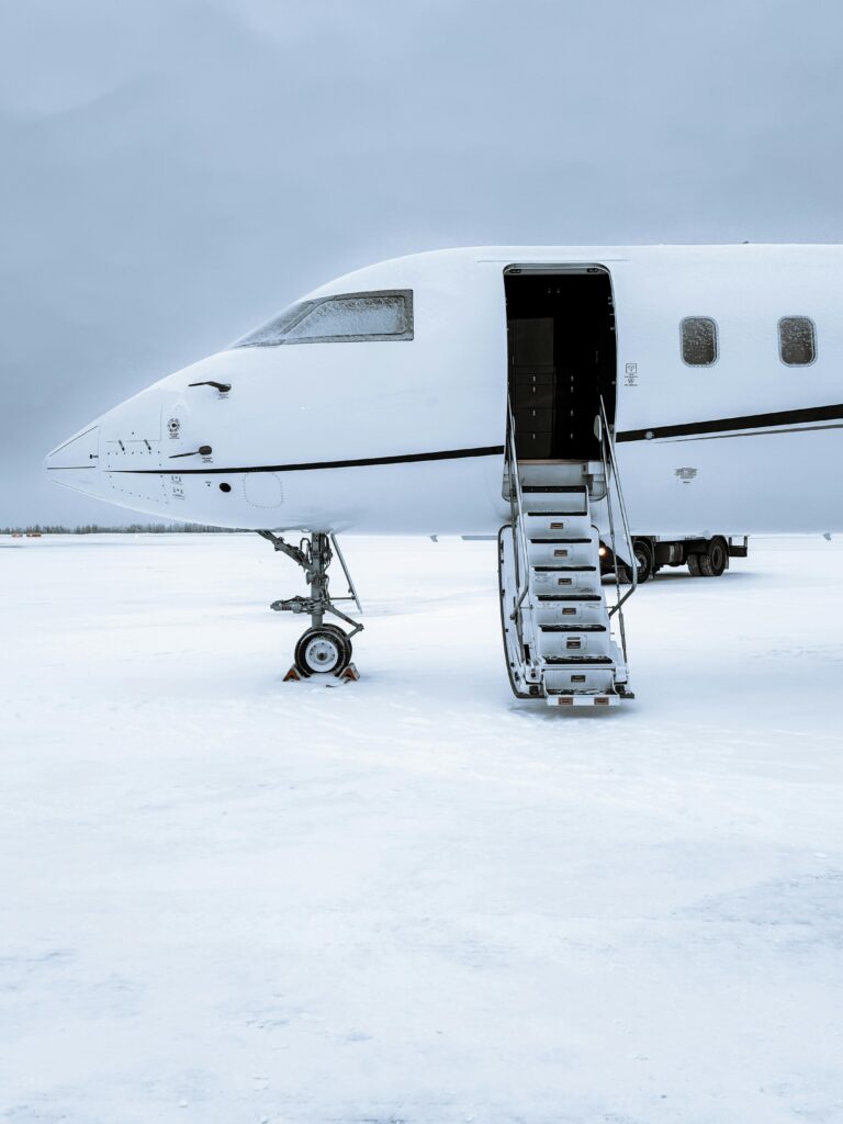 A private jet parked on a snowy runway during winter, with steps extended.