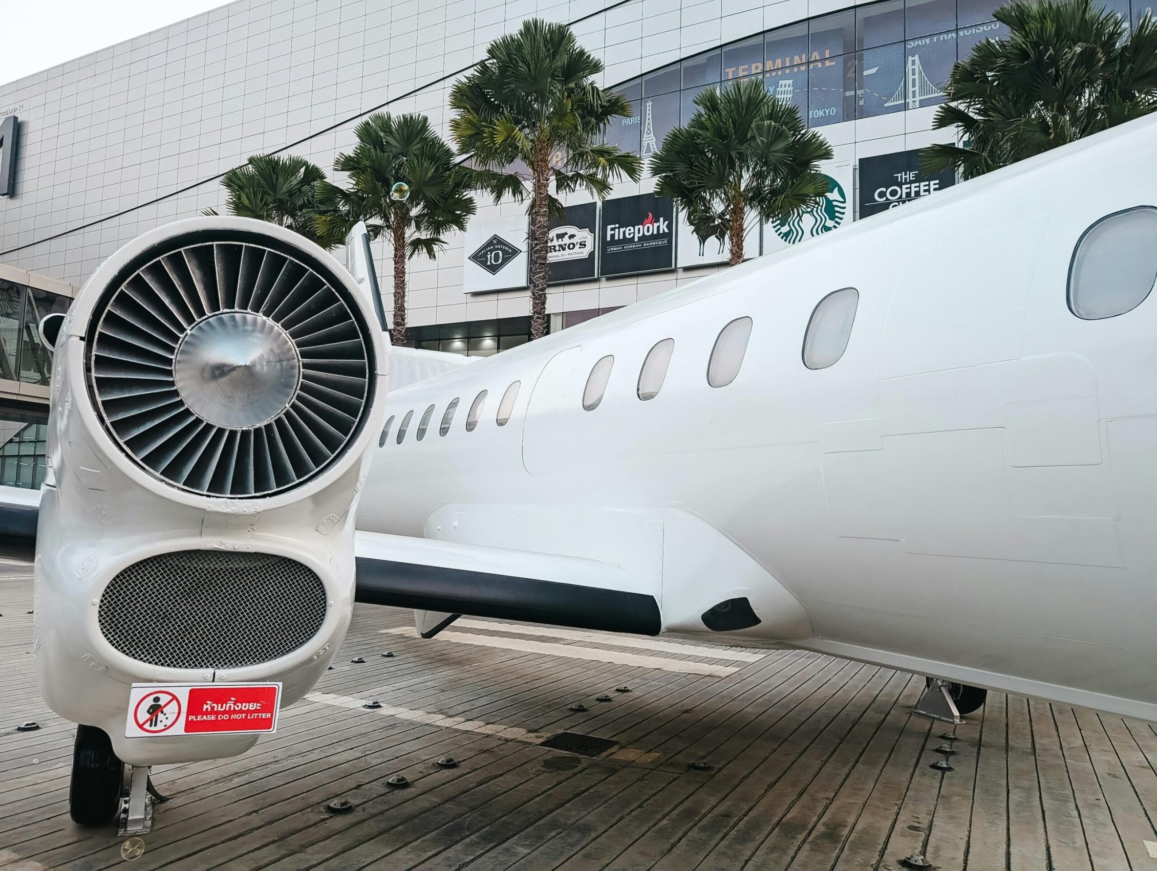 Private jet parked at a modern airport terminal with palm trees and shopping signs visible.